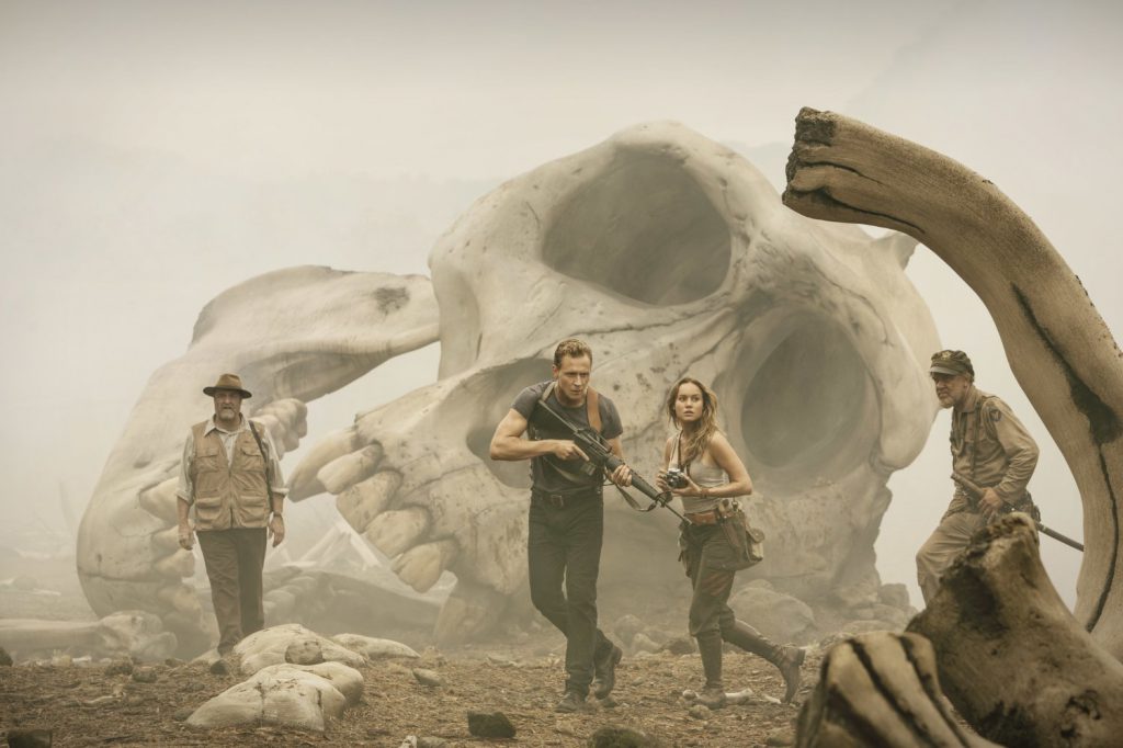 John Goodman, Tom Hiddleston, Brie Larson, and John C Reilly in front of a giant gorilla skull