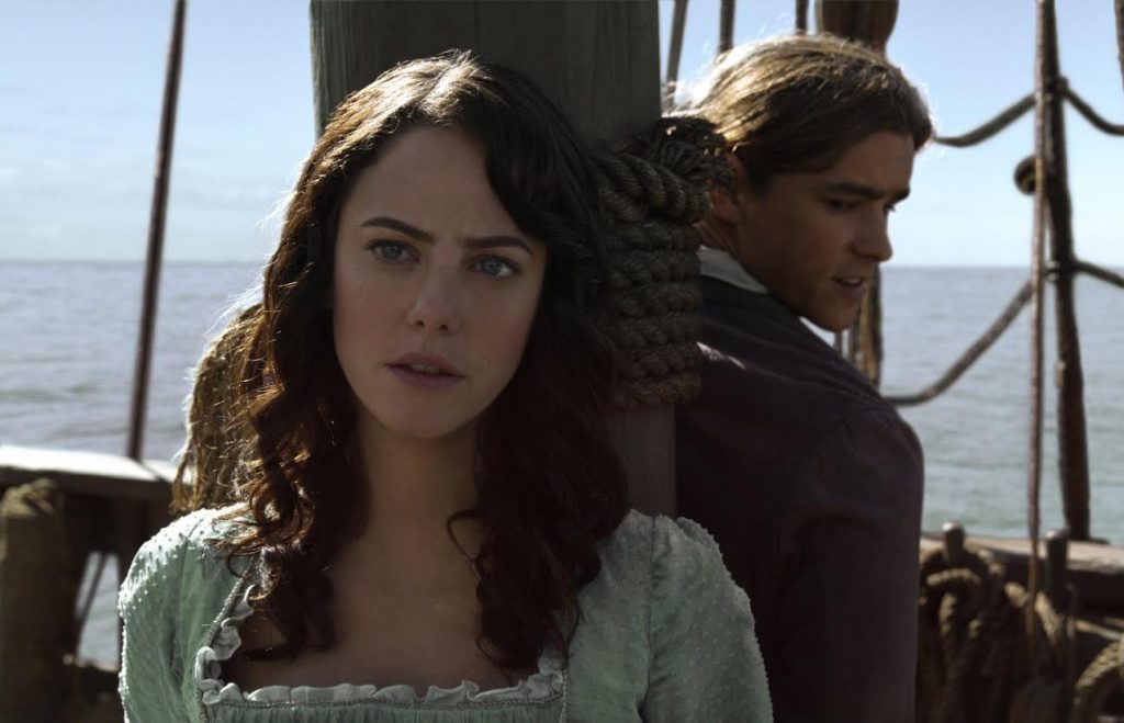 A brunette woman and a blond man are tied to a ship's mast, and are wearing period clothing